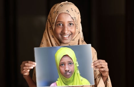 A smiling Maryan holds up a photo of herself from before cleft treatment