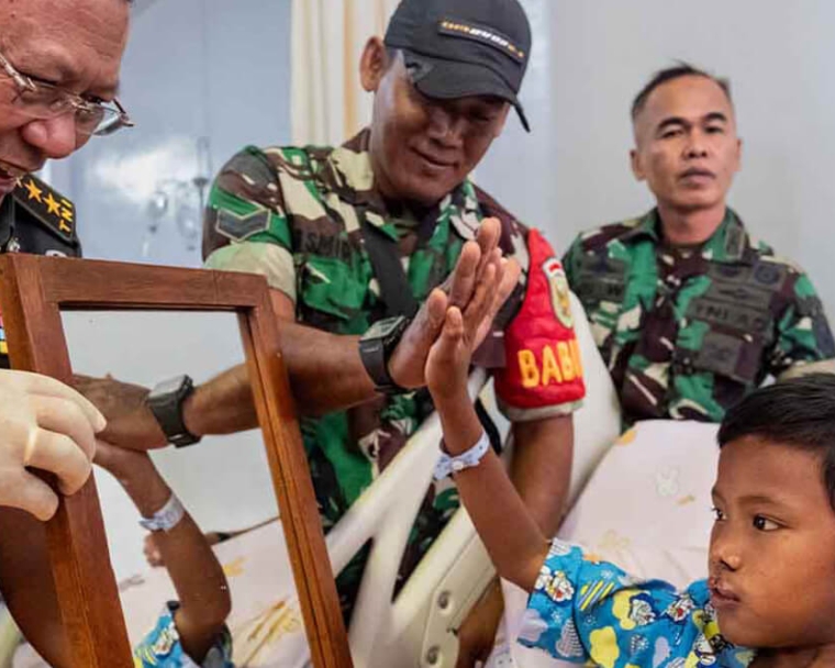 Des soldats indonésiens souriant et donnant des tapes dans la main à Rajib alors qu'il se regarde dans le miroir après sa chirurgie de la fente